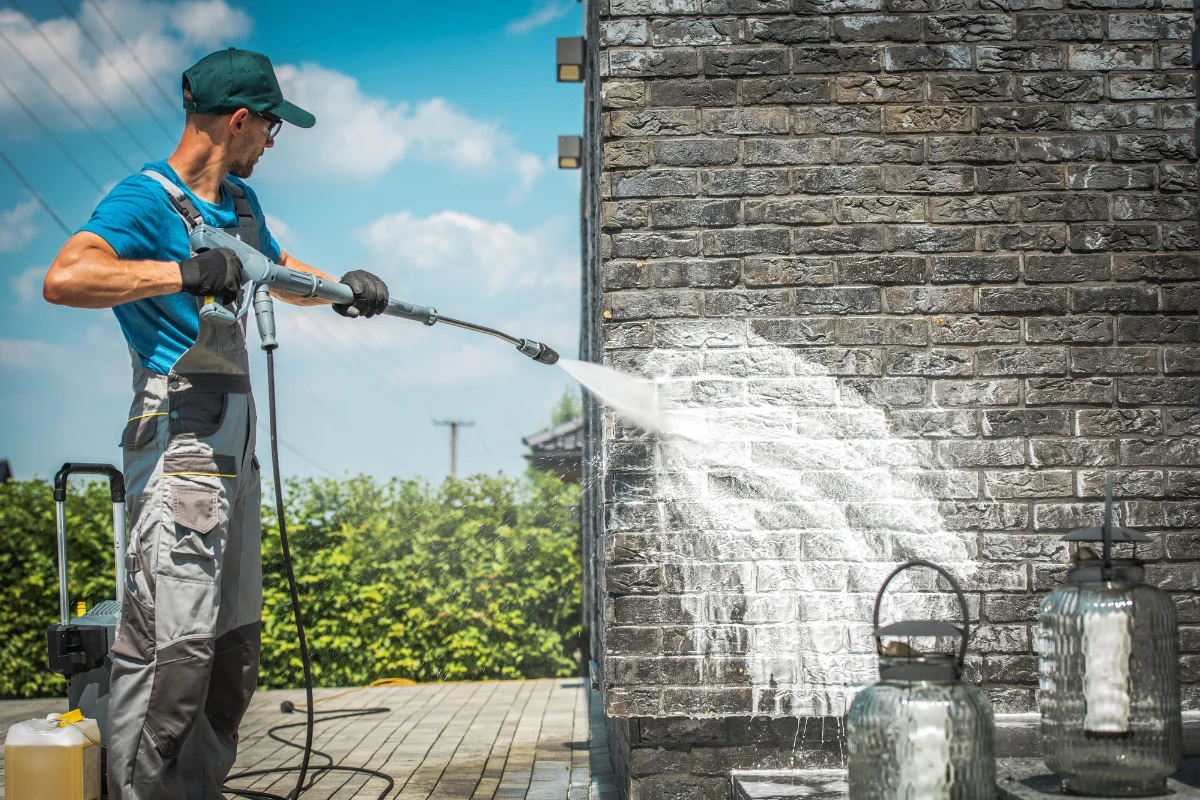 a man using pressure washing machine to clean brick exterior wall of home